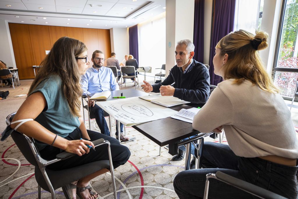Drei Personen sitzen um ein Flipchart herum und diskutieren