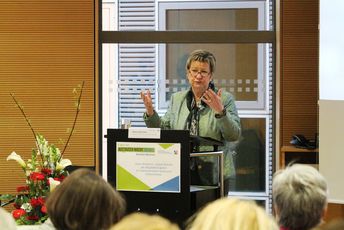 Eine Frau gestikuliert hinter einem Redner/-innenpult