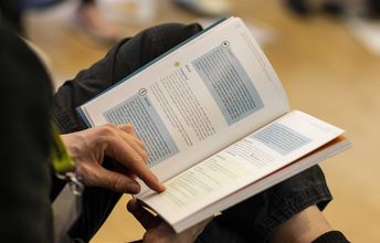 Geöffnetes Buch liegt auf den Knien des Lesenden.