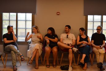 Sechs Menschen sitzen auf Stühlen nebeneinander und unterhalten sich.