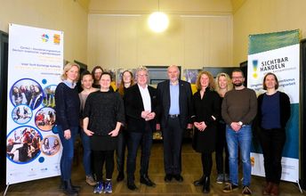 Gruppe von Menschen steht gemeinsam im Flur und schaut in die Kamera