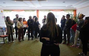 Perspektive auf im Halbkreis stehende Seminargruppe im Gespräch, Vordergrund: Seminarleiterin 