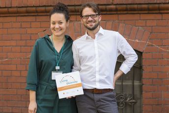 Zwei ConAct-Mitarbeiter*innen halten eine Living Diversity Broschüre in der Hand