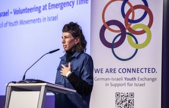 Eine Frau spricht an einem Pult. Hinter ihr ist ein banner mit der Aufschrift "We are connected".