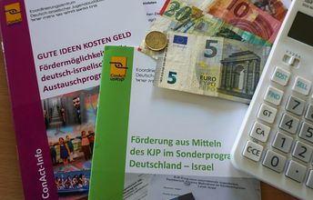 Auf einem Tisch liegen 2 Hefte, ein weißer Stift, etwas Geld und ein Taschenrechner.