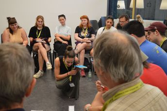 Eine Frau kniet in der Mitte eines Stuhlkreises.