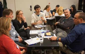 Teilnehmende sitzen an einem Tisch und diskutieren.