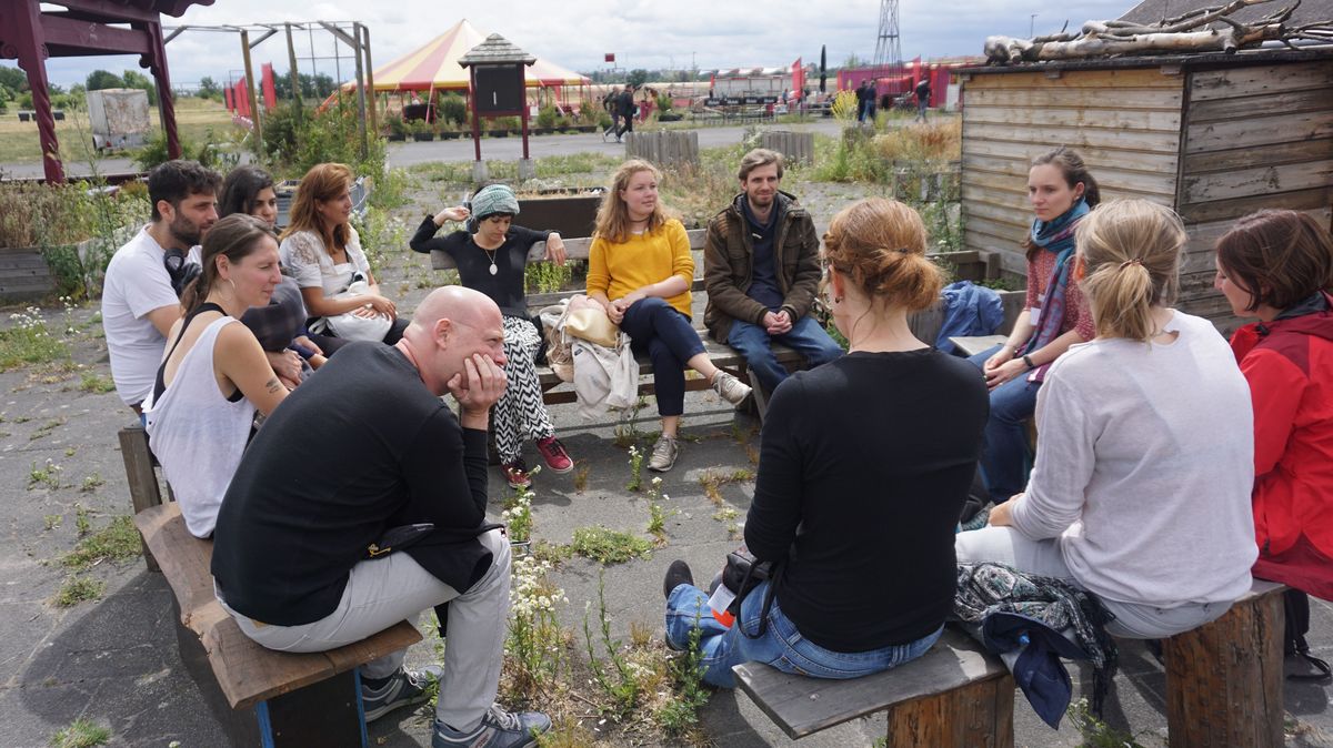 Eine Gruppe junger Menschen sitzt auf Bänken auf dem Tempelhofer Feld in Berlin und unterhält sich