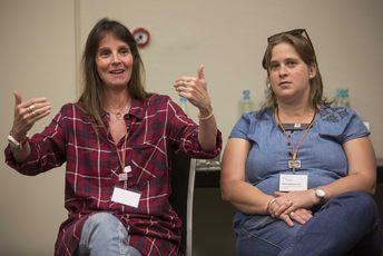 Zwei Frauen sitzen nebeneinander, eine davon gestikuliert mit den Händen