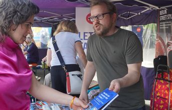 Ein rothaariger Mann zeig einer Frau ein blaues Buch mit der aufschift ,,Education and Encounter after October 7''.