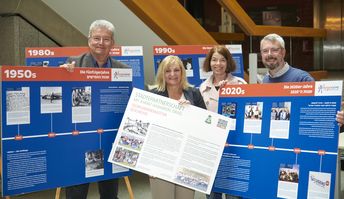 Vier Menschen lächeln in die Kamera und halten blaue und weiße Ausstellungstafeln der Präsentation zu 70 Jahre deutsch-israelischem Jugendaustausch hoch.