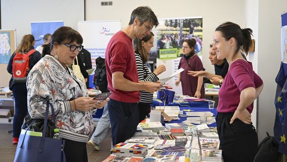 Drei Personen stehen an einem Infostand und schauen sich die Materialien an.