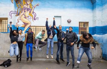 Eine Gruppe Jugendlicher springt vor einem Wandgrafitty in die Luft.