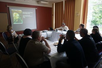 Teilnehmende sitzen um einen Tisch und schauen auf eine Powerpoint präsentation.