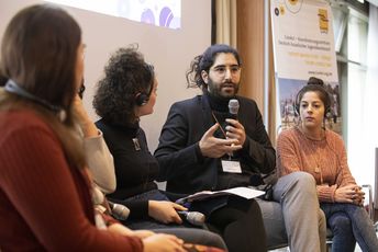 Eine Podiumsdiskussion mit vier jungen Menschen, ein Mann hält ein Mikrofon in der Hand und spricht