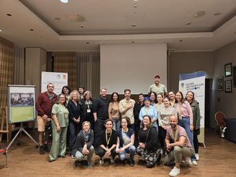 Gruppenfoto mit lächelnden Personen in einem Seminarraum mit Bannern im Hintergrund.