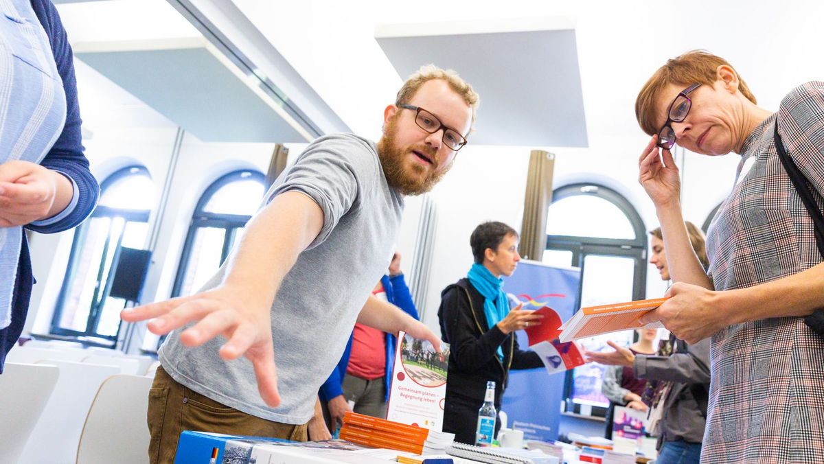Ein ConAct-Mitarbeiter erklärt einer Frau etwas am Infotisch