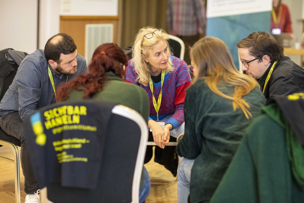 Gruppe von Frauen und Männern sitzt in einem Stuhlkreis im konzentrierten Gespräch vertieft einander zugebeugt.
