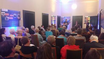 Viele Menschen sitzen auf Stühlen und hören der Band "Blaue Stunde" zu.