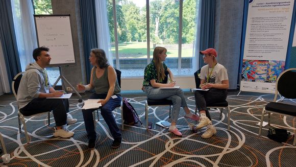 Personen sitzen in Zweiergruppen zusammen und sind im Gespr&auml;ch.