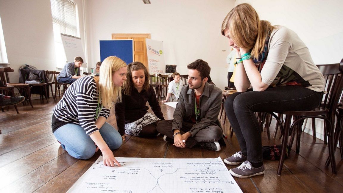 Vier junge Leute sitzen um ein großes Flipchart-Papier herum und reflektieren