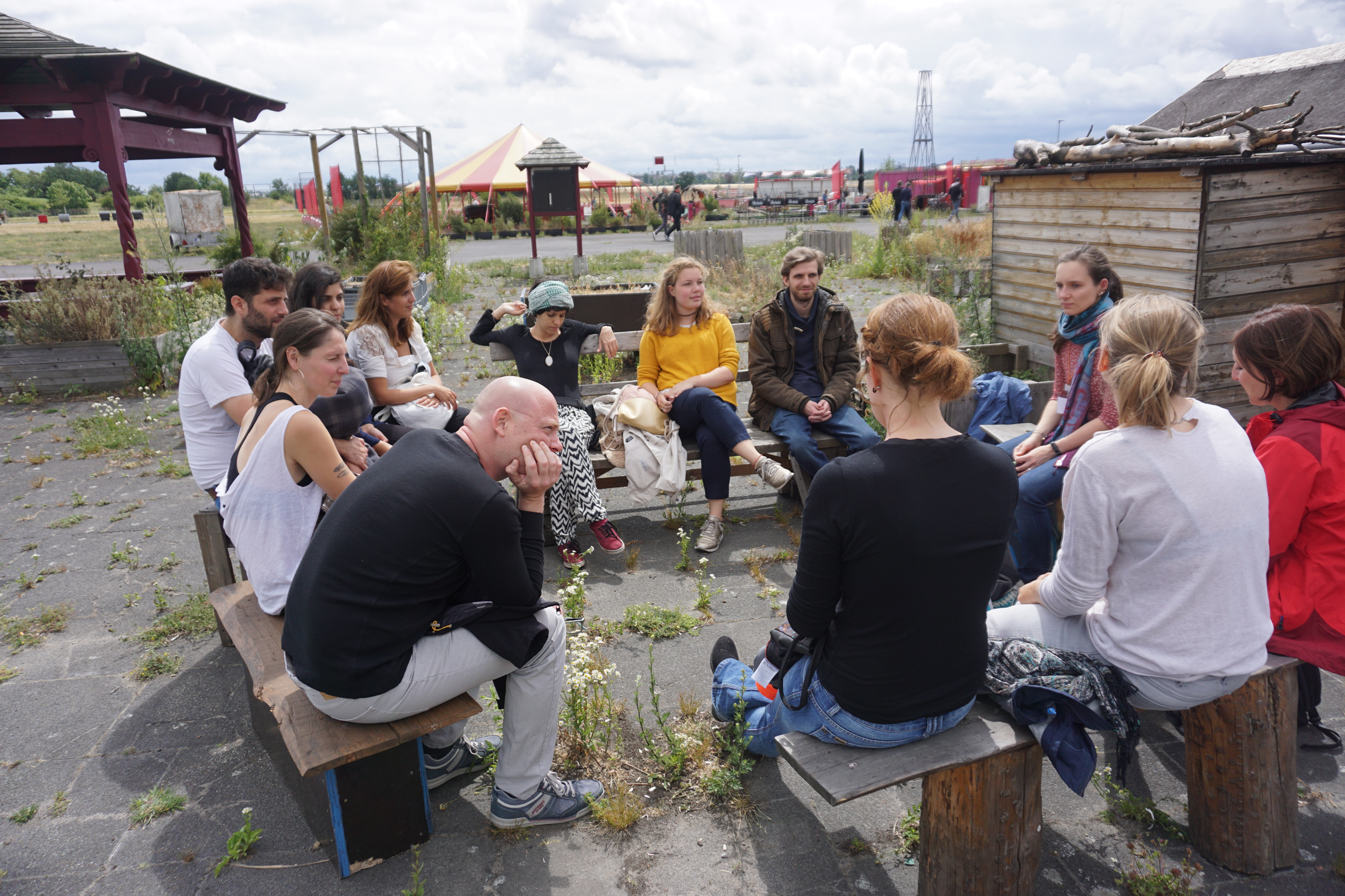 Eine Gruppe junger Menschen sitzt auf Bänken auf dem Tempelhofer Feld in Berlin und unterhält sich