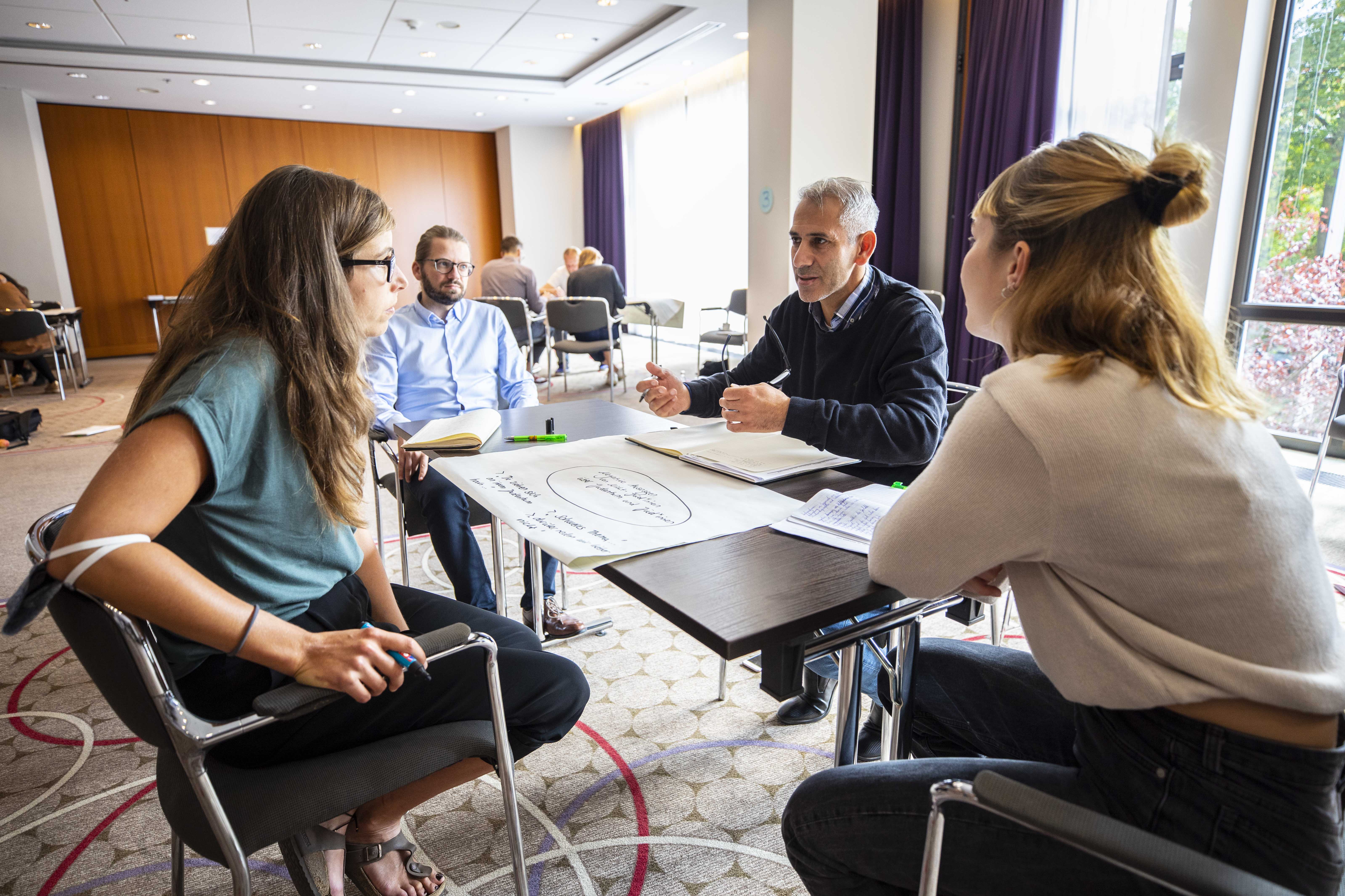 Drei Personen sitzen um ein Flipchart herum und diskutieren