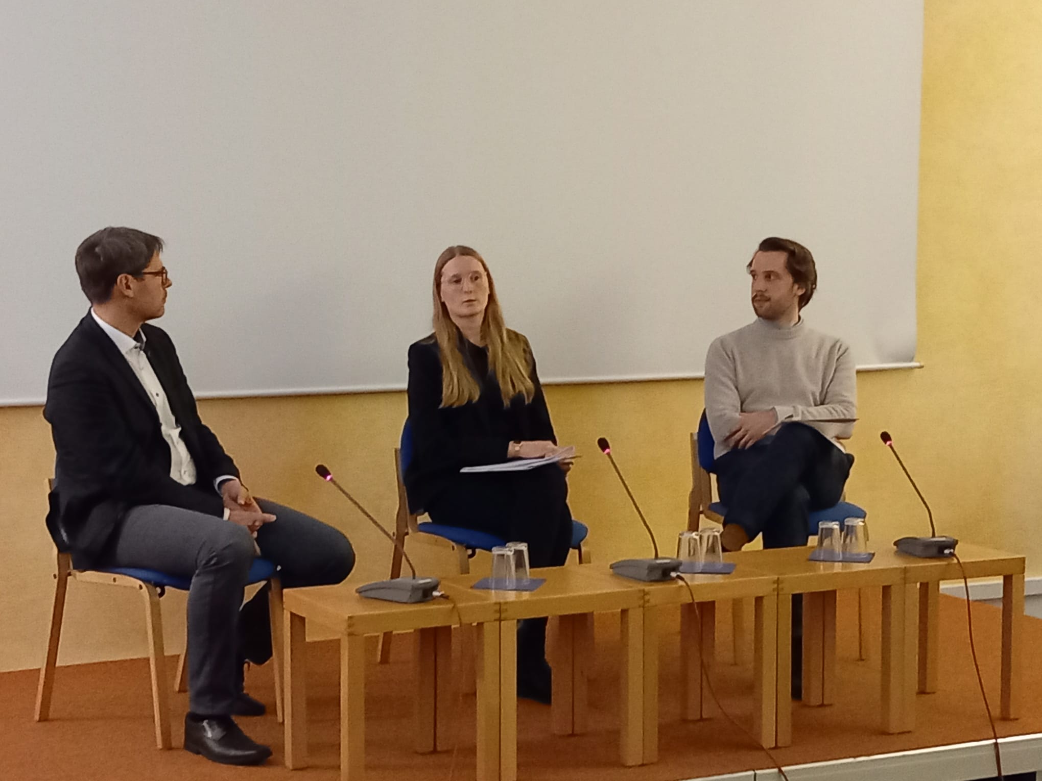 Drei Personen sind auf einer B&uuml;hne im Gespr&auml;ch.