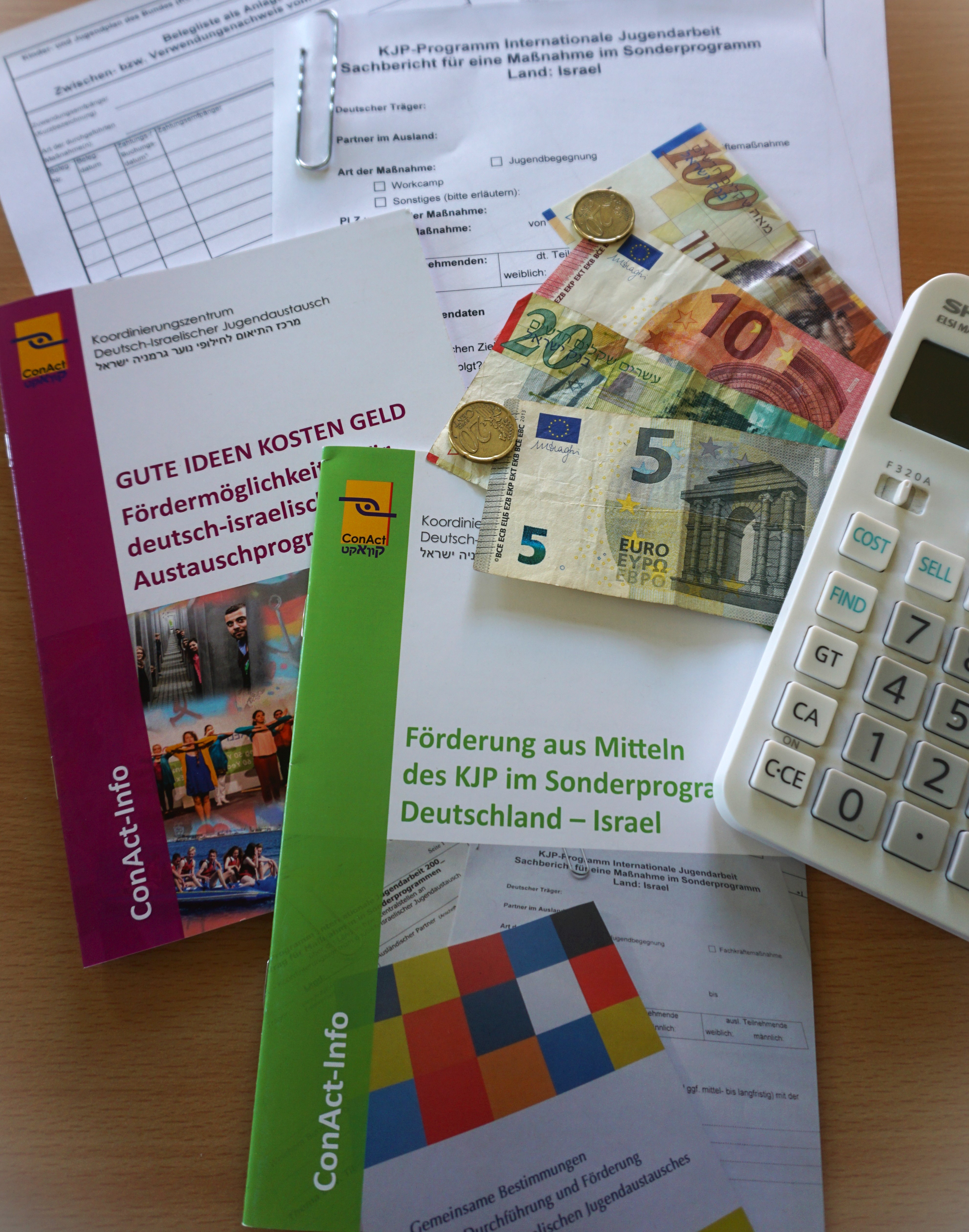 Es sind Infohefte, Formulare zur F&ouml;rderung des deutsch-israelischen Jugendaustauschs, Geldscheine und M&uuml;nzen (Euro und Schekel) sowie ein Taschenrechner zu sehen.