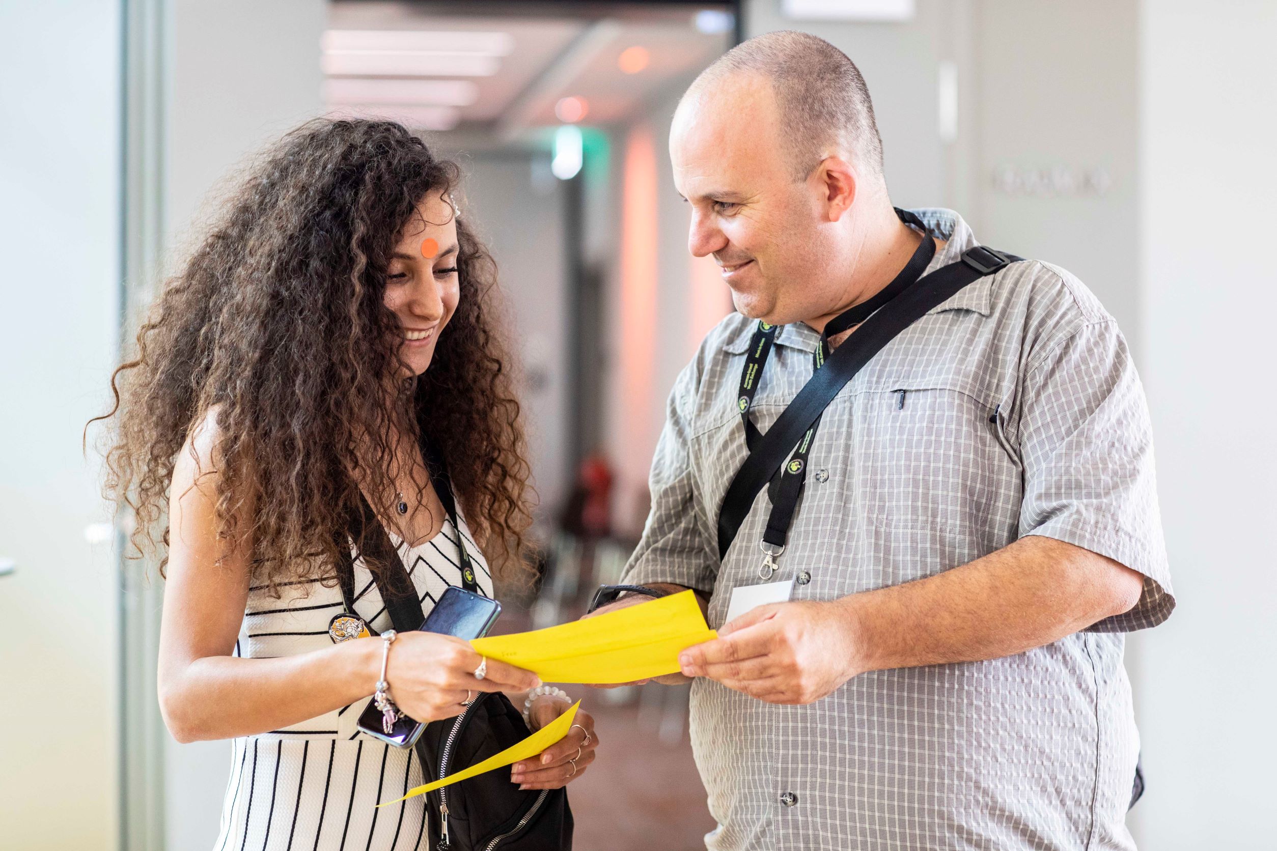 Eine Frau und ein Mann stehen zusammen und schauen auf ein gelbes Blatt Papier