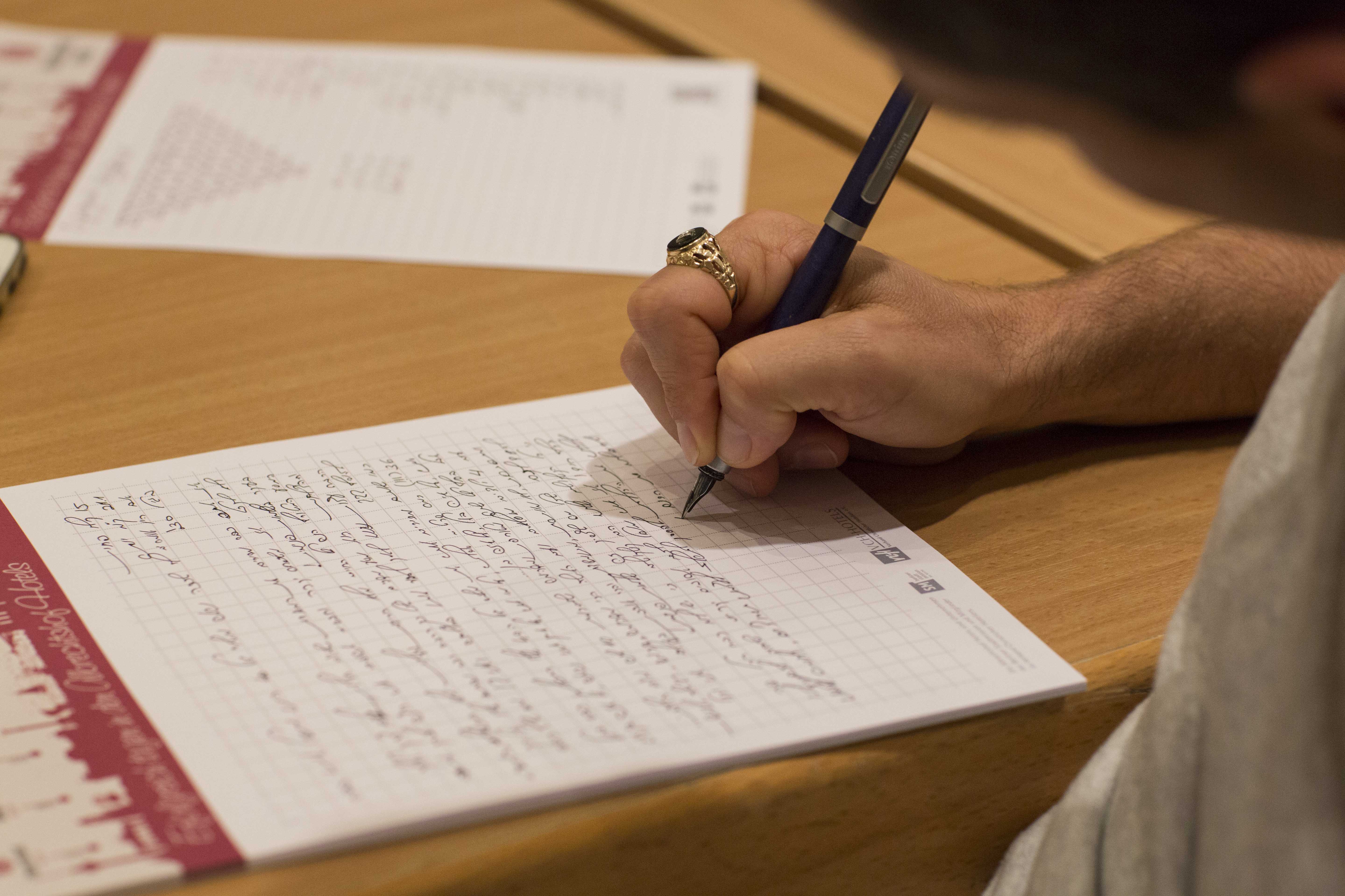 Jemand schreibt einen hebräischen Text auf ein Blatt Papier