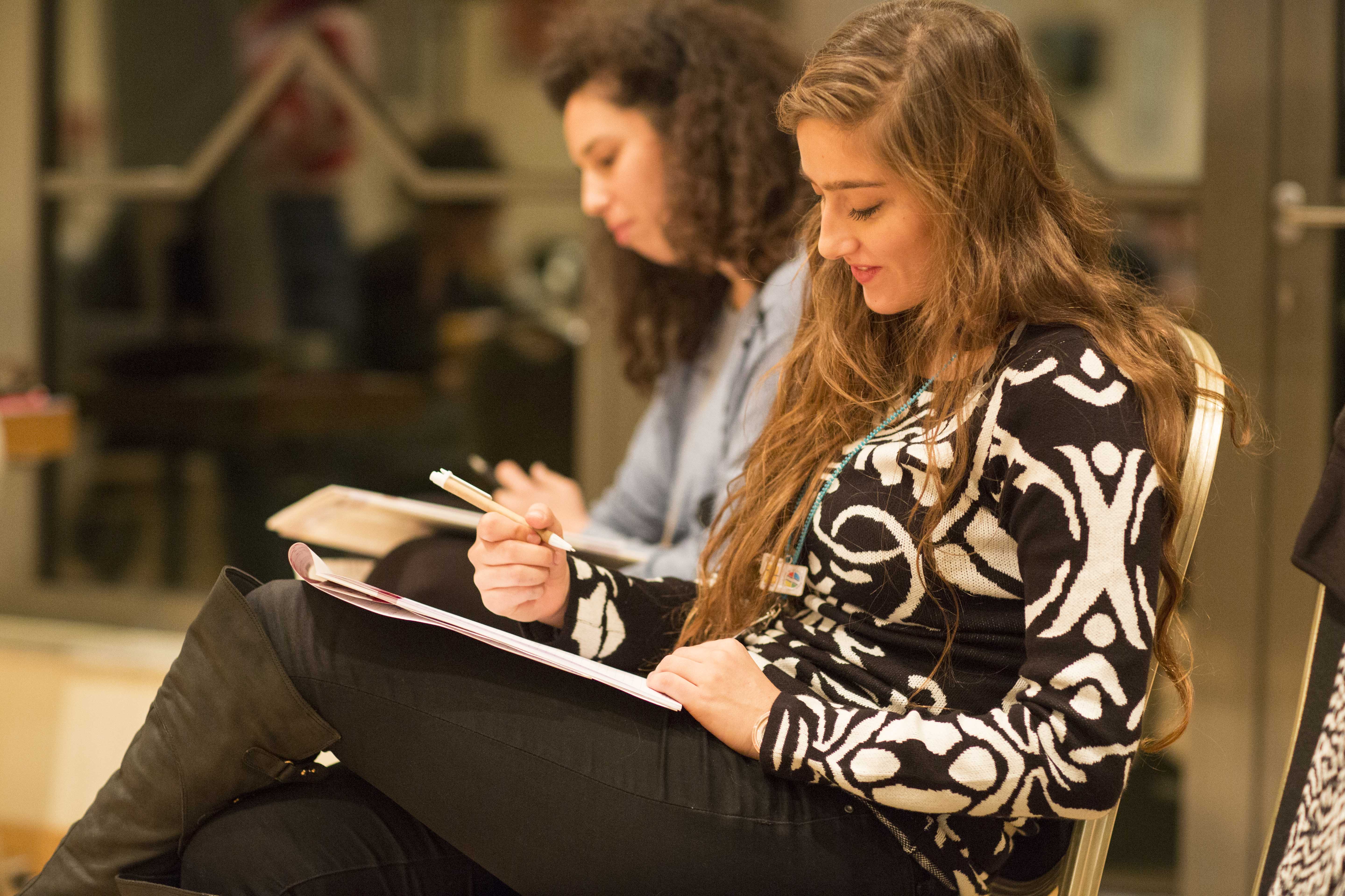 Zwei sitzende Frauen, eine davon schreibt in ein Notizbuch